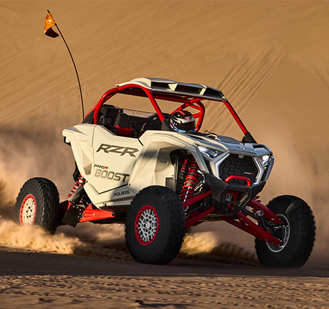 RZR Pro R Boost kicking up dust on a desert dune at sunset